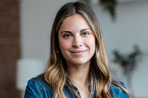 Portrait of beautiful young woman looking at camera while standing in the living room at home.