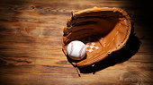 Baseball ball in a glove on the wooden table.