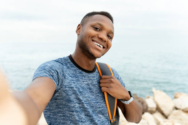 istock Mixed race man smiling to the camera while making selfie with backpack at his smartphone 1472766907
