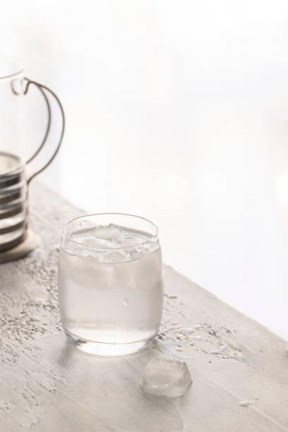 istock Glass with refreshment Water with ice cubes and jar on white table.Copy space 1472767571