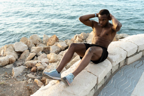 istock Young mixed race man exercising on the beach and doing sit ups with concentrated face 1472767987
