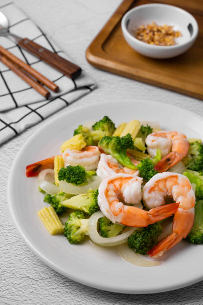 istock Fried broccoli and shrimp with oyster sauce, onion and corn in white dish on concrete table. 1472774681