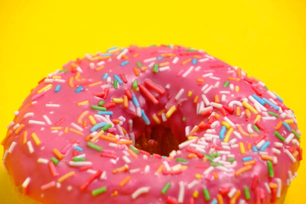 istock Donut with pink icing and multicolored sugar sprinkles.On yellow background,closeup. 1472776608