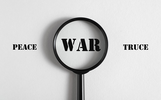 War and peace concept. Printed words peace, war, truce and a magnifying glass on a white background.