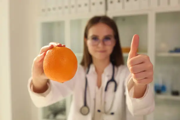 Photo of Doctor nutritionist holding orange in his hands and showing thumbs up closeup