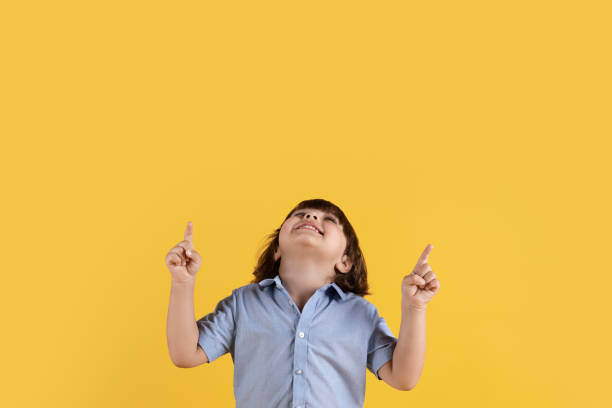 istock Cute little boy looking upward and pointing with both hands, enjoying interesting promo, orange background, empty space 1472783218