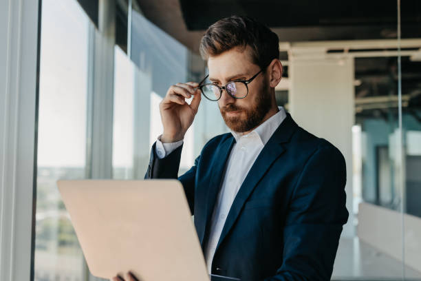 istock Focused businessman looking at laptop computer, working in modern office, reading emails from his business partners 1472783229