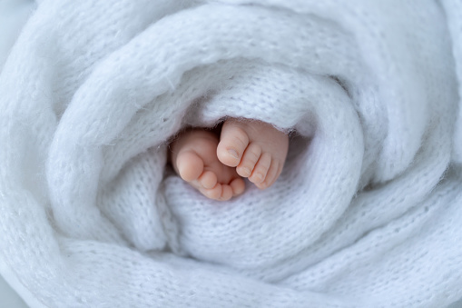 newborn baby's legs wrapped in white soft cloth close up.