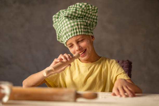 The boy sits on the table, makes dough, plays and sings.