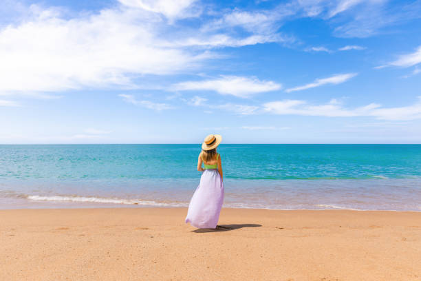 istock Cheerful woman in a straw hat standing alone on sandy beach 1472786933