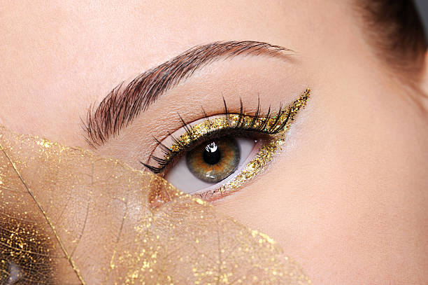 Female eye with a golden arrow make-up Macro shot of beauty  female eye with golden eyeliner make-up covered artificial yellow  leaf eyeliner stock pictures, royalty-free photos & images