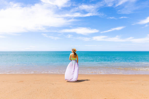 istock Cheerful woman in a straw hat standing alone on sandy beach 1472787693
