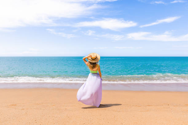 istock Cheerful woman in a straw hat standing alone on sandy beach 1472789382