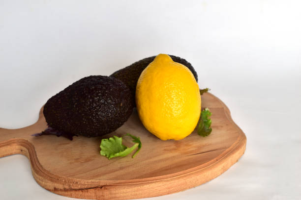 There are two avocados and one lemon on a cutting board.