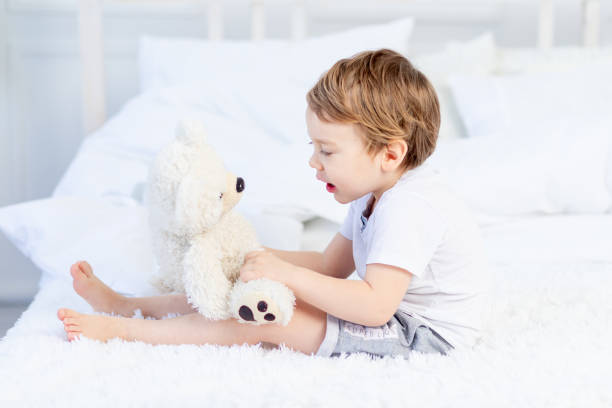 istock baby with a teddy bear on the bed at home playing 1472793261