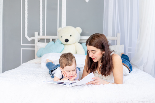 mom reads a book to the child or teaches him at home on the bed Happy loving family. Mom and son