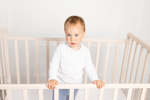 small baby boy 2 years old in the crib looking at the camera in the bright children's room, the child after sleeping