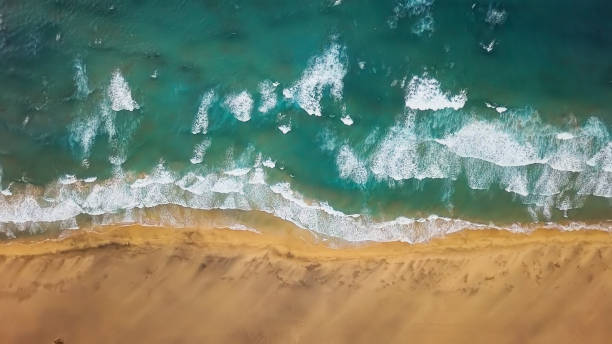 Overhead aerial view of ocean waves splash against desert sand beach Playa de Cofete, Jandia Peninsula on Fuerteventura, Canary Islands, Spain stock photo