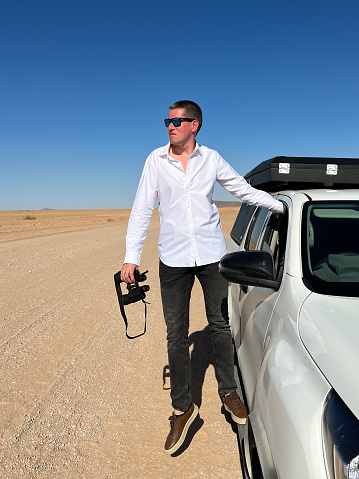 Car on gravel dirt road in desert. Sandy landscape, nobody. Wildlife in Africa. SUV Toyota Hilux white automobile vehicle. Man driver traveler with binoculars