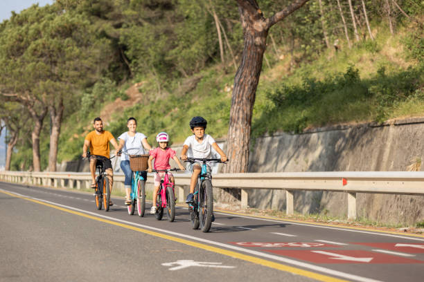 istock Two kids with parents riding bikes along a sea coastline, front view 1472798518