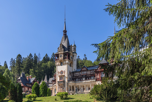 Sinaia - Romania. July 15, 2022: Beautiful tandem of majestic vivid centuries-old nature and human creations Peles Castle skillfully and delicately inscribed in the environment