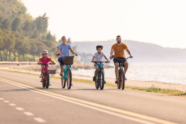 istock Two kids with parents riding bikes along a sea coastline, front view 1472798800