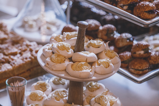 Meringue dessert Pavlova cakes with vanilla custard and cream on a wooden service stand at a celebration buffet