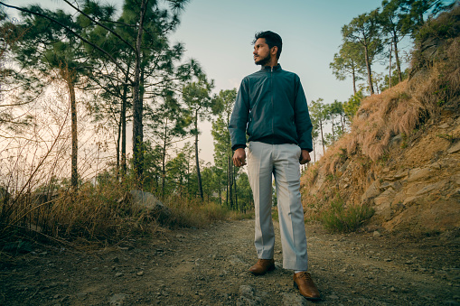 An Asian/Indian young man walks on a dirt road and looks at the view at sunset in the tranquil mountain of Himachal Pradesh, India.