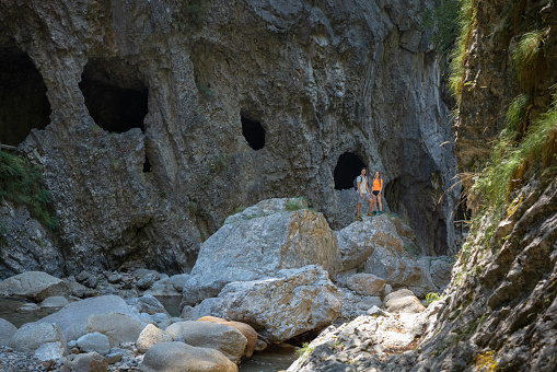 Hiker couple jumping on the rocks while crossing mountain river, passing a walking tour through the gorge. Travel and adventure lifestyle concept.