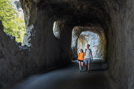 Couple of Young Happy Travelers Hiking with Backpacks on the Beautiful Trail and Rock Tunnel