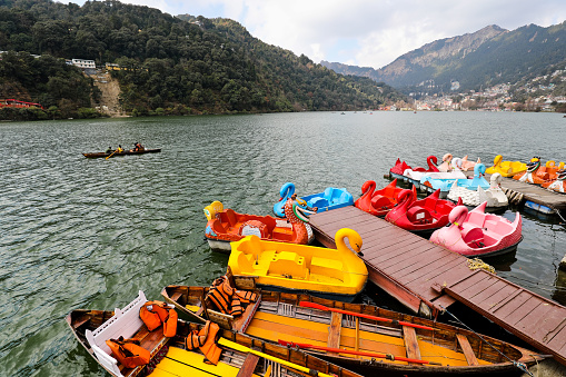 Nainital UK India - December 25, 2022 : Tourist enjoying sunny winter morning at Naini Lake in Nainital in UK India. The pabble and rowboats are moored at the jetty.