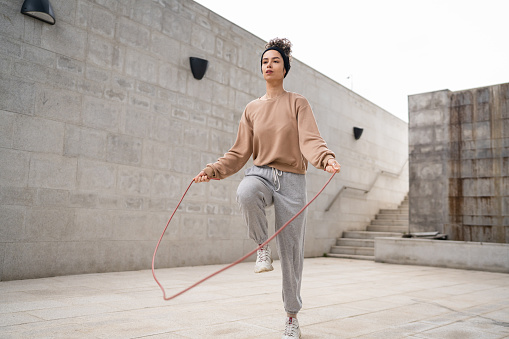one woman young adult caucasian female jumping rope training concept beautiful sporty generation Z in day outdoor with headphones on her head copy space real person jump full length