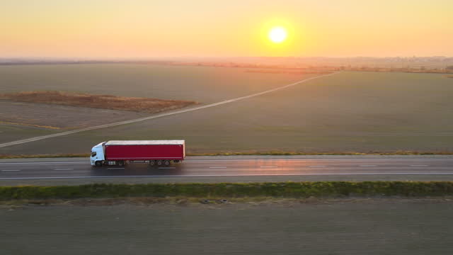 Aerial view of semi-truck with cargo trailer driving on highway hauling goods in evening. Delivery transportation and logistics concept