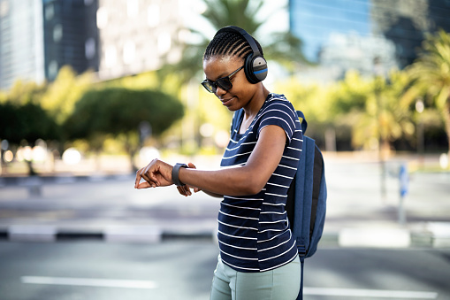 Female with headphones check her smart watch while walking in the city with a backpack