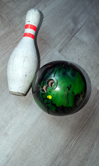 Top down view of a worn and broken green bowling ball and used pin on a greay defocused floor.