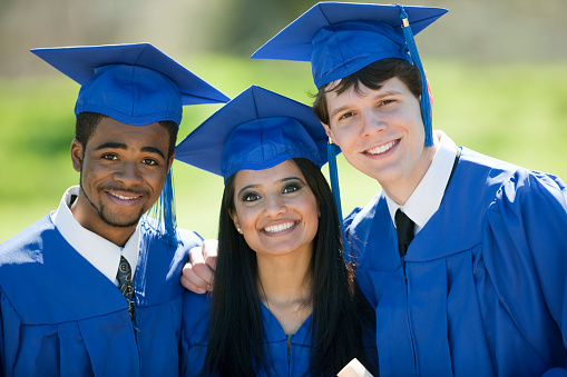 Three young people wearing graduation caps and gowns smiling for the camera on graduation day.