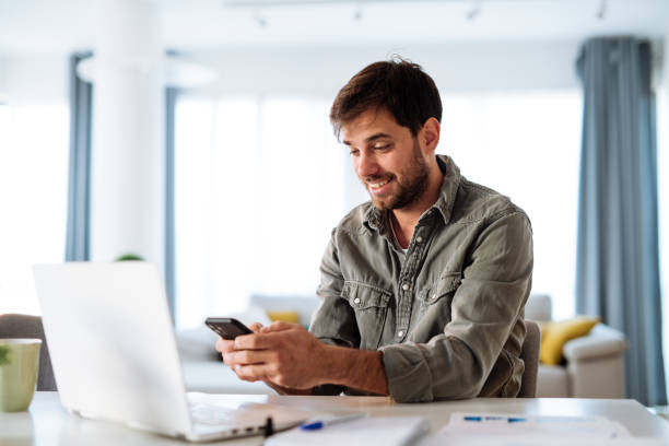 istock Mid adult man working from home on laptop and using smart phone 1472823621