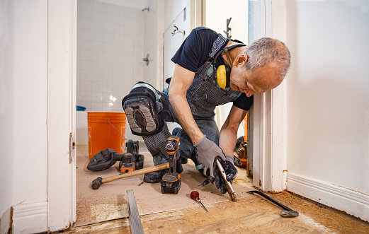 Senior Caucasian man doing construction renovation indoors. He is dressed in work clothes with jeans overall and t-shirt. Interior of private home during renovation, located in North America.