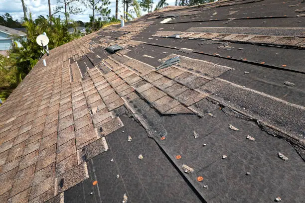 Photo of Wind damaged house roof with missing asphalt shingles after hurricane Ian in Florida. Repair of home rooftop concept