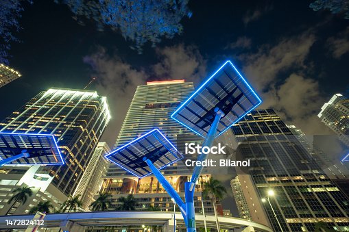 istock Blue solar photovoltaic panels mounted in modern city on street poles for electricity supply of streetlights and surveillance cameras. Futuristic energy source in downtown Miami, Florida 1472824112