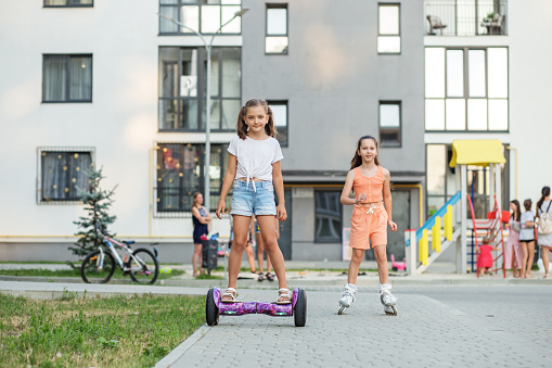 Happy children riding on hoverboards or gyro scooters outdoors in summer. Roller skating. Active life concept