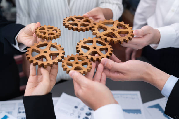 istock Closeup top view hands holding gears over table with BI reports for harmony. 1472826031