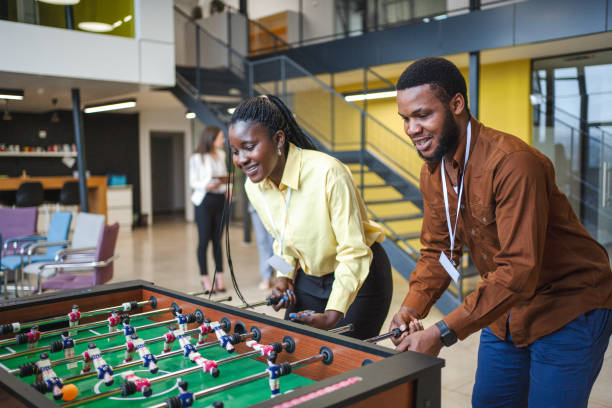 istock Two black business colleagues having fun while playing foosball on a break from work 1472828902