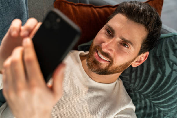 istock Top view of the caucasian man typing on smartphone keyboard while lying at sofa and working at home 1472829405