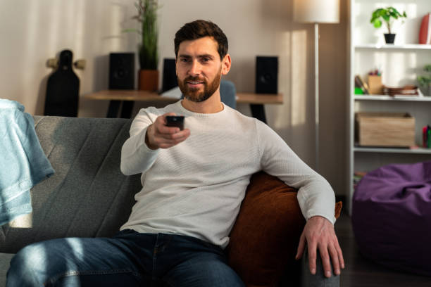 istock Man dressed in casual clothes lying on the sofa in home and holding remote control while watching TV 1472829502