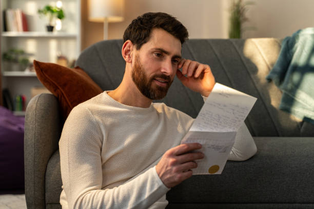 istock Caucasian man feeling happy while reading his letter from relatives and sitting at floor near sofa 1472829587