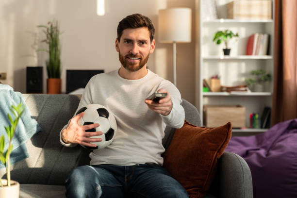 istock So exciting. Young interested guy sitting on sofa and expressing exhilaration while watching game 1472829681