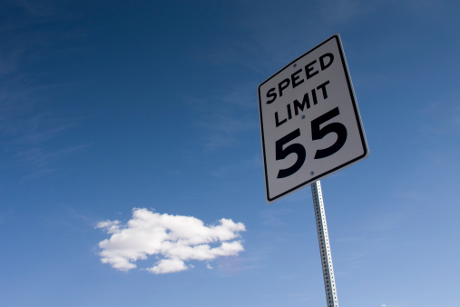 A 55 mph speed limit sign under a bright blue sky, joined by a lonely cloud cluster. Space for copy.