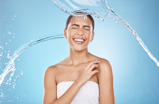 Woman skincare, laughing or water splash on blue background studio for shower healthcare wellness, Brazil hygiene maintenance or self care grooming. Happy smile, beauty model and cleaning water drop