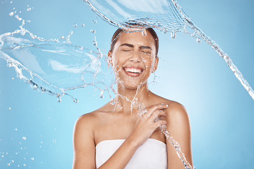 Happy woman, laughing or water splash skincare on blue background studio in healthcare wellness, Brazil hygiene maintenance or self care grooming. Smile, beauty model or cleaning water drop in shower